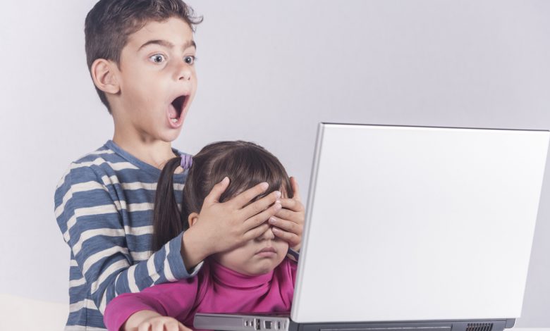 older child blocking eyes of younger child from seeing the computer screen