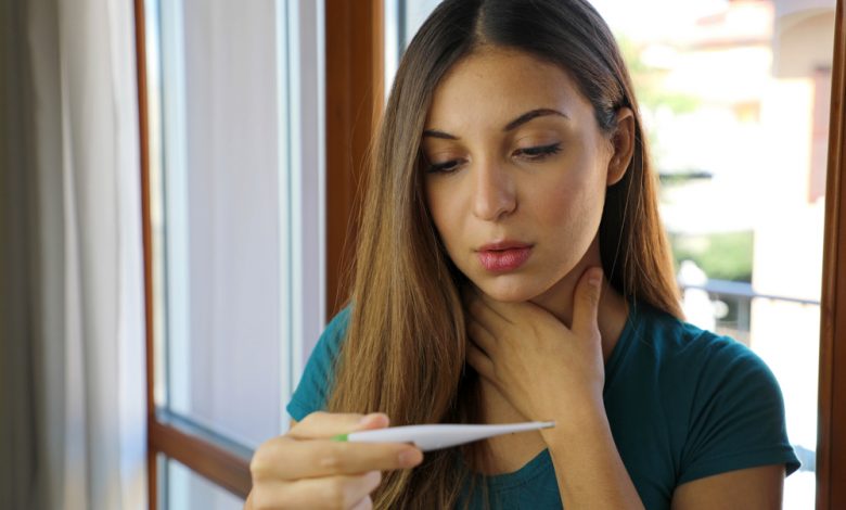 A woman checking her temperature with a thermometer.