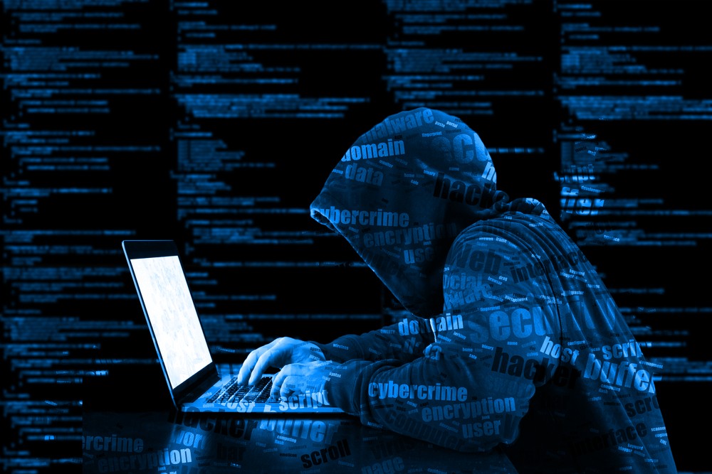 Hacker in a blue hoody standing in front of a coding background.