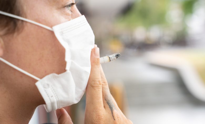 Person smoking a cigarette while wearing facemask.