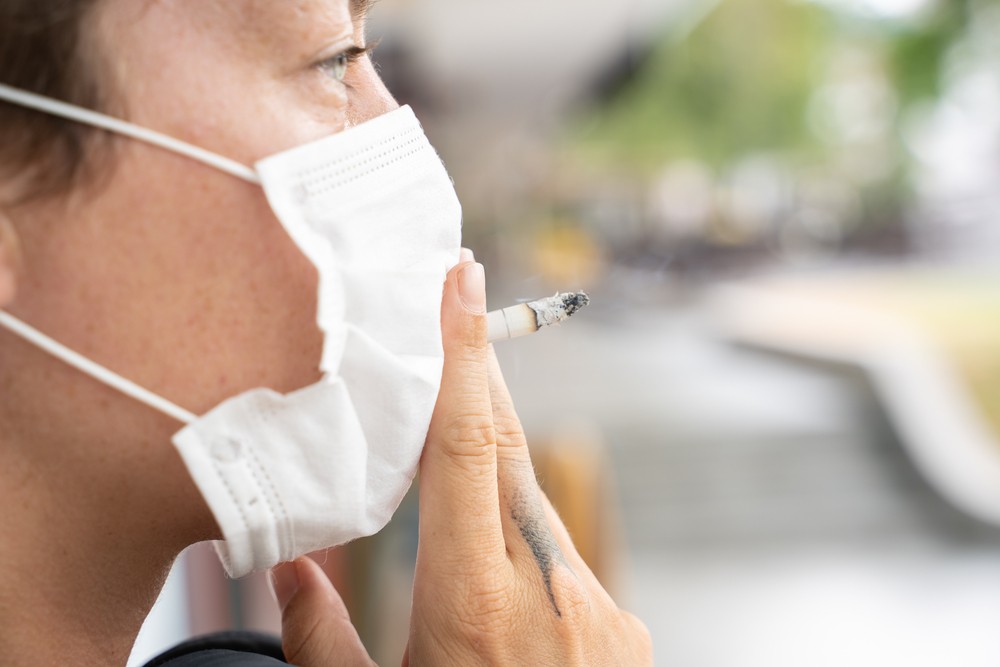 Person smoking a cigarette while wearing facemask.