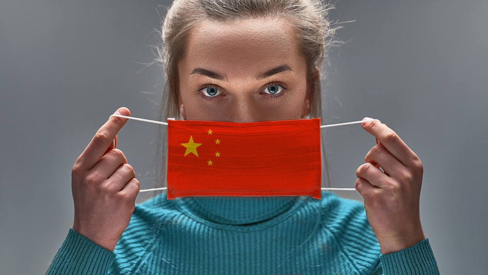 Image of women putting on face mask with the design of a China's flag.