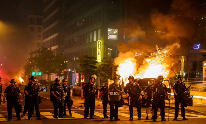 A group of policemen forms a line in front of a burning car.