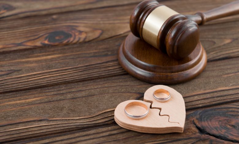 Divorce concept showing wedding rings on the figure of a broken heart from a tree, hammer of a judge on a wooden background.