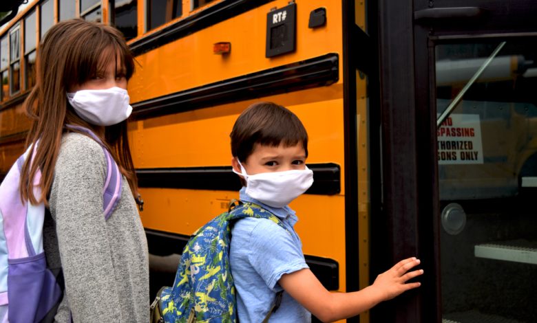 Boy and girl, students, children wearing face masks getting on school bus.