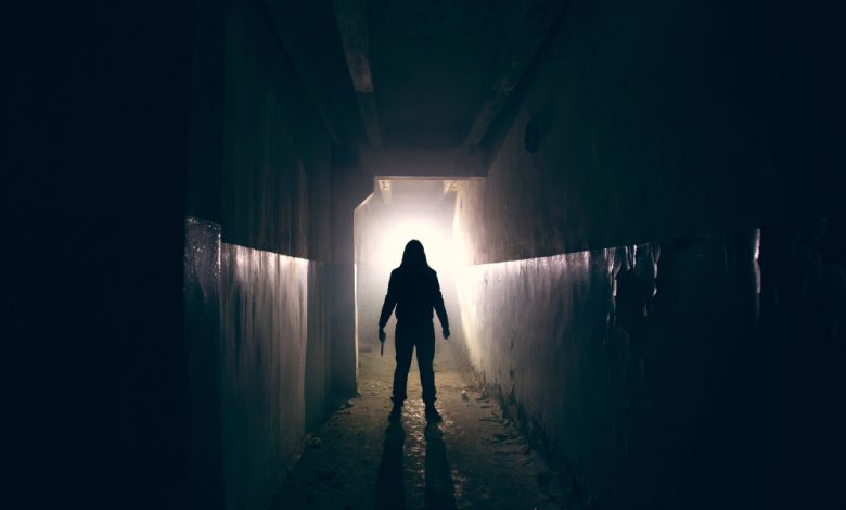Silhouette of maniac with knife in hand in a long dark corridor.