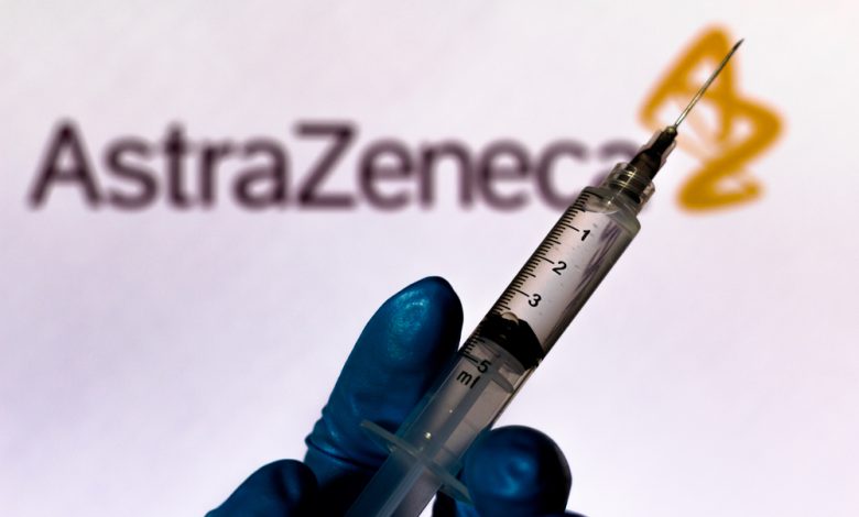 Vaccine held in front of AstraZeneca’s company logo.