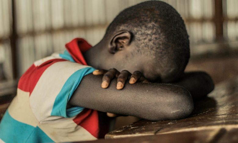 Image of Nigerian boy with his head resting on a school desk.