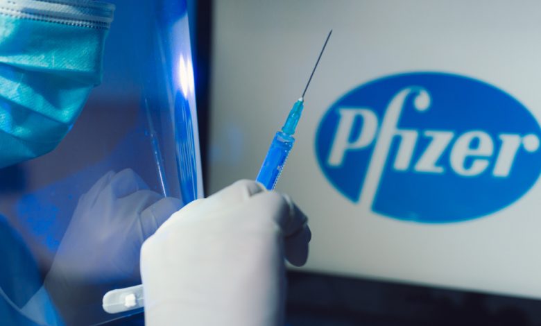 Image of a Hand holding covid-19 vaccine with Pfizer logo in the background.
