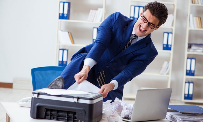 Businessman angry at printer jamming papers.