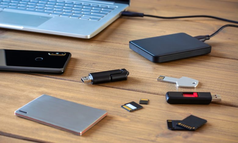 Usb sticks, external hard drive, SD cards, mini and micro SD cards, laptop and smartphone on a table next to a laptop.