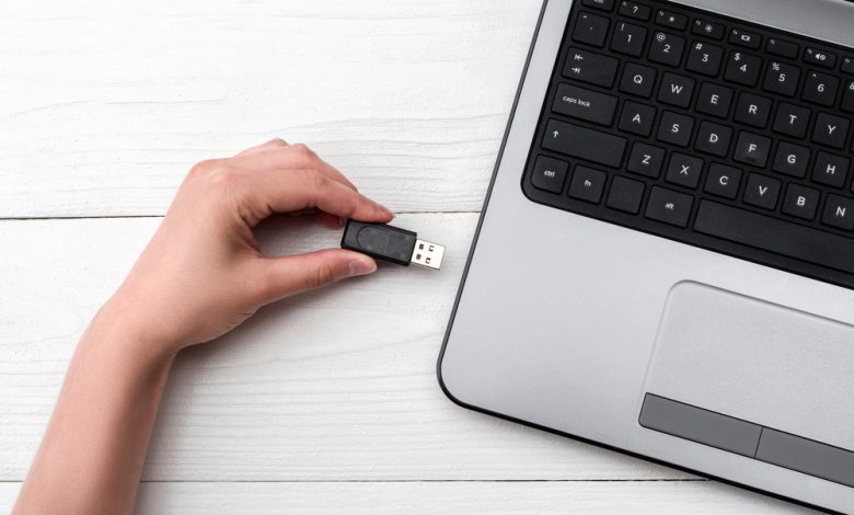 Hand inserting USB flash drive into laptop computer on white background.