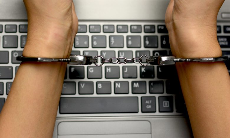 Hacker concept, punishment for cybercrime with one person in handcuffs above notebook keyboard.