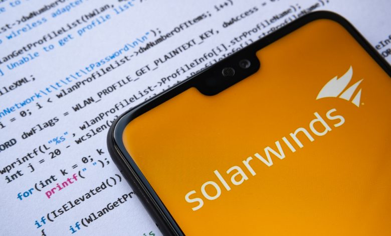 Solarwinds logo seen on the smartphone screen, with simple C attack code on the paper background.