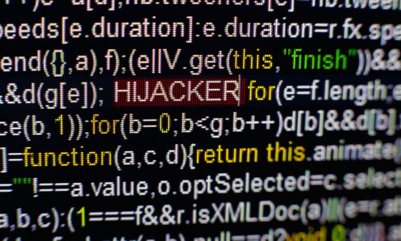 Macro photo of computer screen with program source code and highlighted HIJACKER inscription in the middle. Script on the screen with virus in it. Cyber security concept. Technology background.