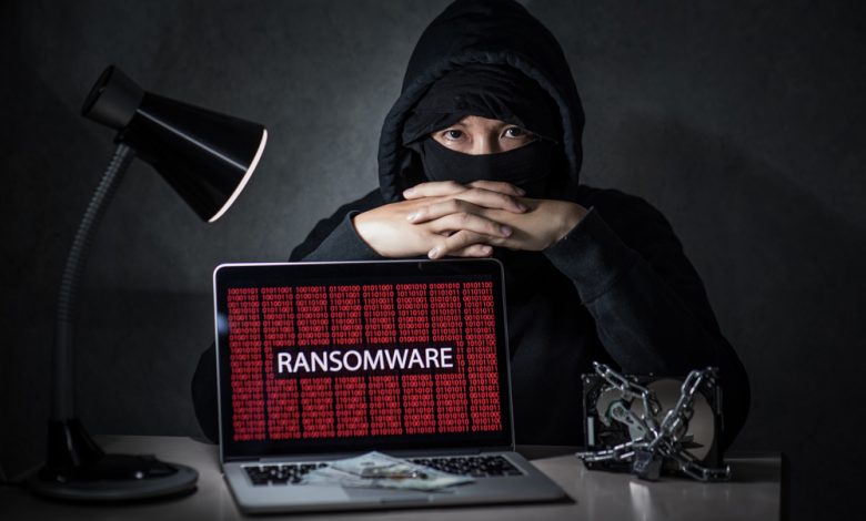 Hacker with computer screen showing ransomware attacking, alert in red digital binary background with hard disk drive lock. Cyber attack concept