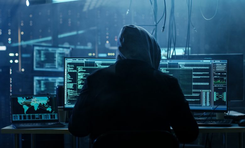 Dangerous Hooded Hacker Breaks into Government Data Servers and Infects Their System with a Virus. His Hideout Place has Dark Atmosphere, Multiple Displays, Cables Everywhere.